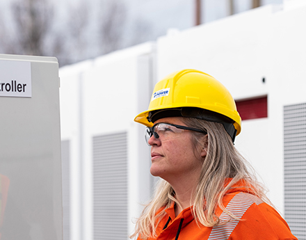 NS Power worker in safety gear standing in from of grid batteries