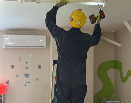 Person in a hard hat using a power drill on an overhead light